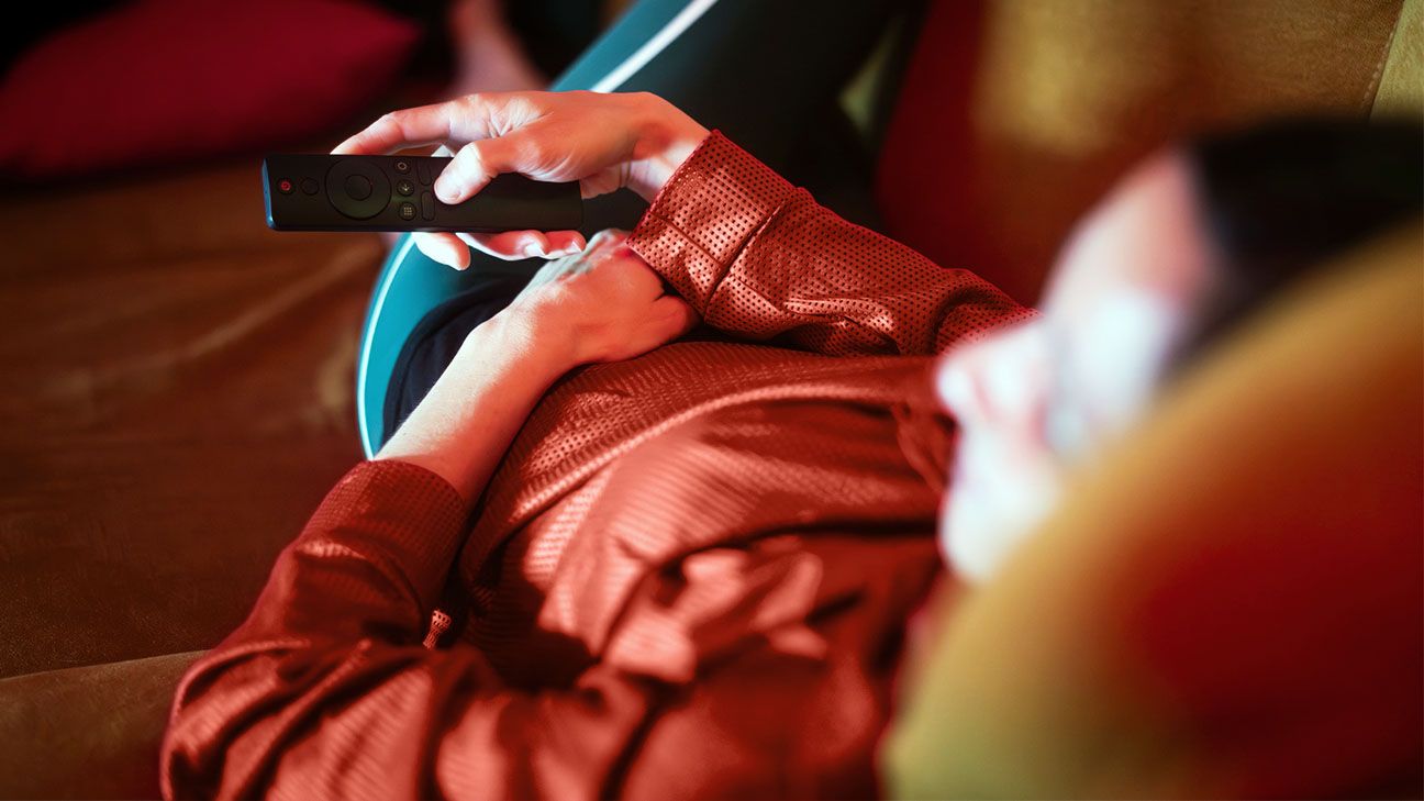Person laying on a sofa with a remote control in their hand