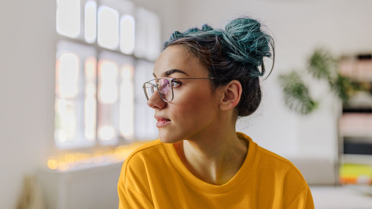Female with blue hair gazes out a window