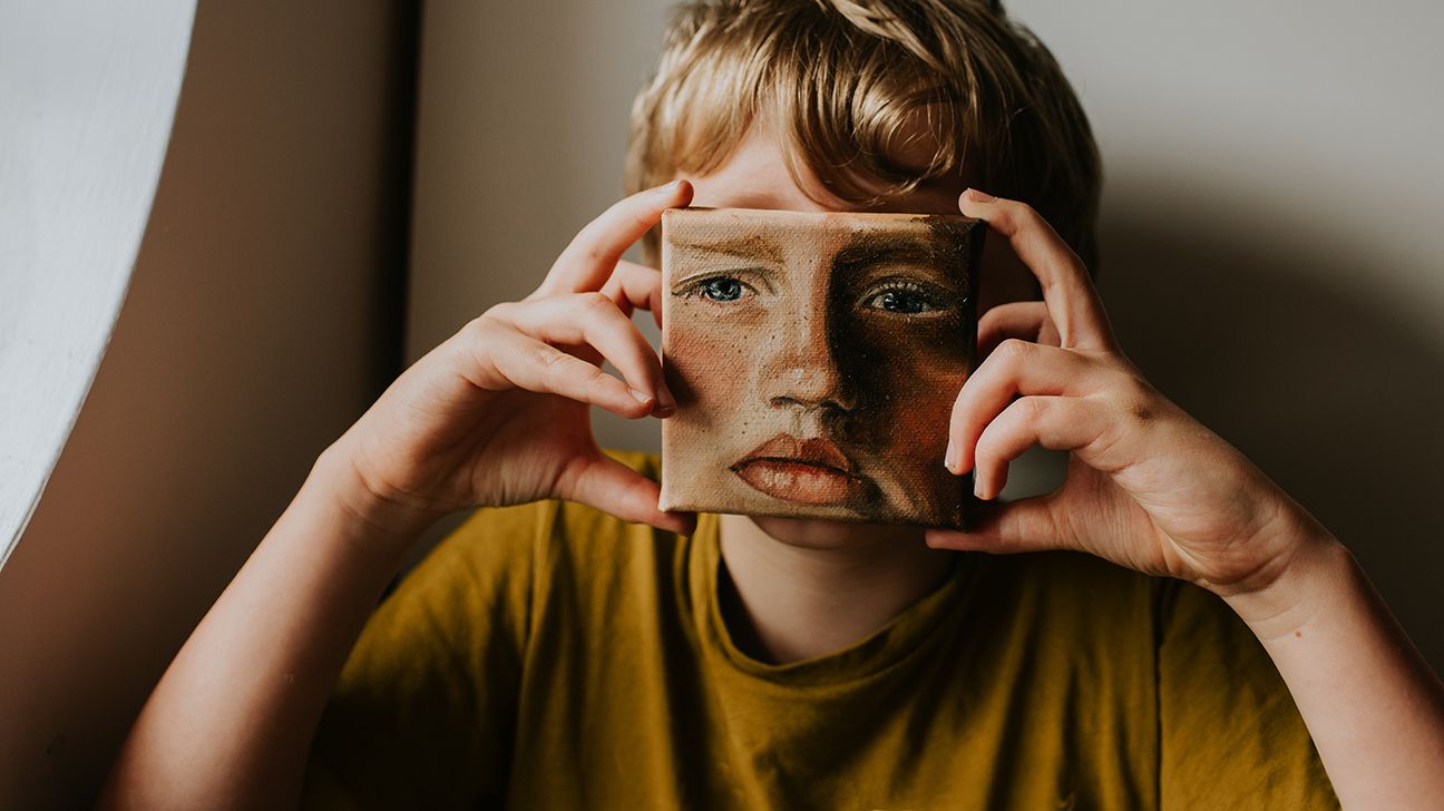 child holding a painting of a sad face in front of their face