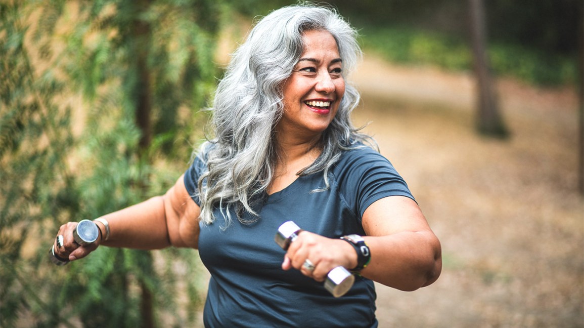 smiling woman lifting dumbbells outdoors